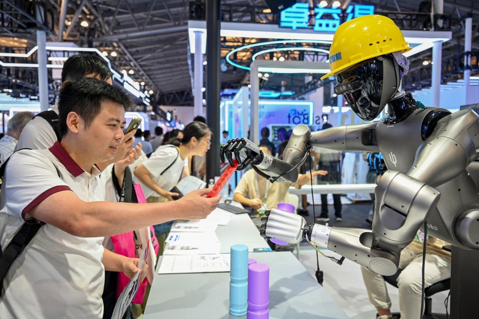 Pessoas assistem a um robô executando tarefas em uma exposição durante a Conferência Mundial de Inteligência Artificial em Xangai， em 26 de julho de 2025. — Foto: Foto da AFP